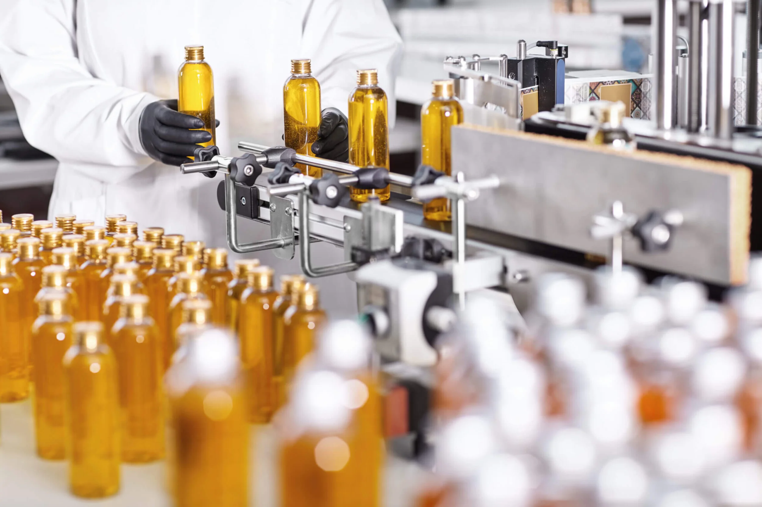Working conditions on factory. Factory worker standing near belt conveyor putting bottles with shampoo on it. Mass production of cosmetics products on modern factory. Ready merchandise on production